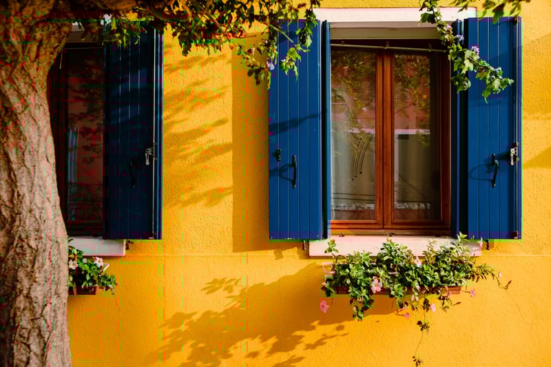 windows-with-blue-shutters-of-yellow-colored-dwell-2023-11-27-05-33-24-utc